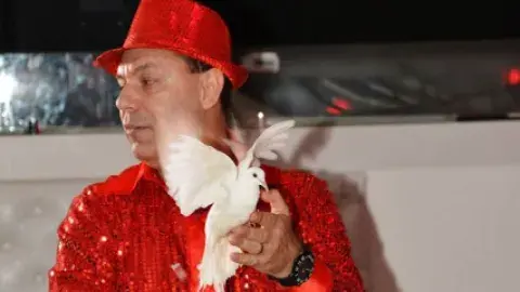 Magician Stoil Stoilov wearing red shirt and hat. Holding a dove and a piece of red cloth
