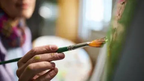 Person holding paint brush and painting on a canvas with paint.