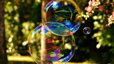 Two large, iridescent soap bubbles floating outdoors in front of a sunny garden background. royalty free photo form pixabay.