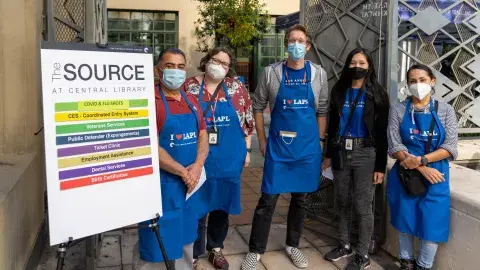 library staff wearing blue aprons stand next to sign that reads The Source