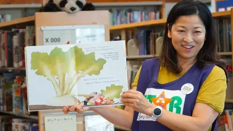 STAR volunteer holding up a picture book to read to an audience