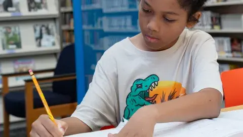 child writes in notebook at library table