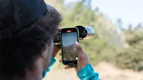 person recording view of nature through binoculars on their smart phone