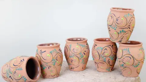 Six small, terracotta-colored ceramic cups, painted with teal and lime green swirling patterns.
