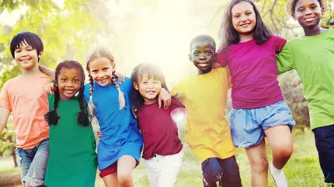 Six children in a row, smiling, wearing colorful shirts, with trees in the background.