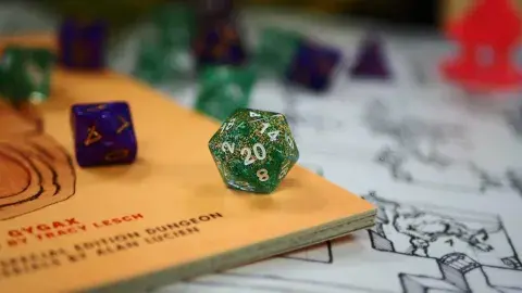 Twenty sided dice centered with many other dice scattered around it, all on top of a map/game rulebook