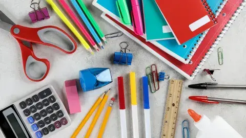 A collection of brightly colored school supplies, like notebooks, scissors, pencils, markers, a ruler, glue, pens, an eraser, and a calculator.