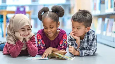 Three kids reading a book together on the floor.