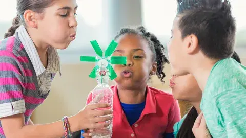 Children blowing on a pinwheel attached to  water bottle