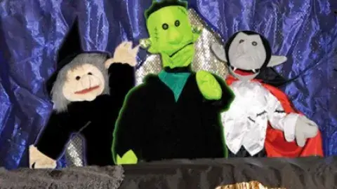 Witch, monster, and vampire puppets in front of a purple curtain