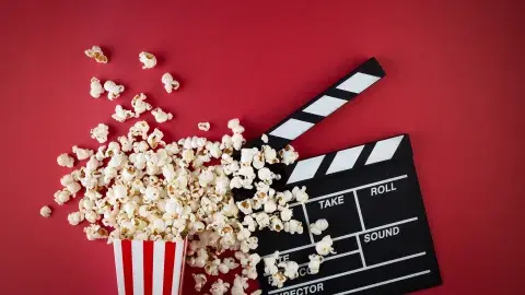 Over-flowing popcorn box next to a film clapper.
