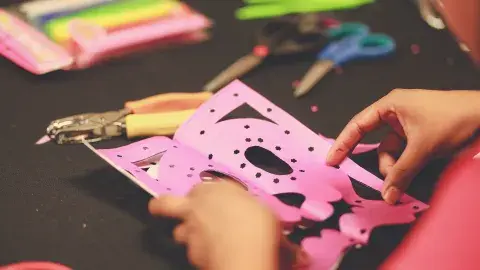 Hands holding tissue paper cut to look like a skull with crafting tools spread around it