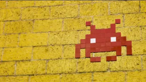 an alien aka "a space invader" created with red tiles on a yellow brick wall