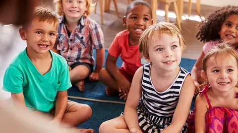 Group of young kids sit on floor rugs listening to a story