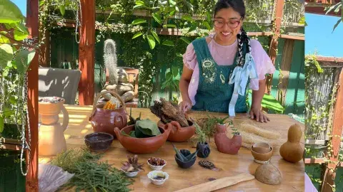 Artist Taty Hernandez stands behind a table of ceramic bowls and vases.
