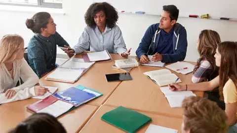 group of seven teenagers sitting around a table mid-discussion