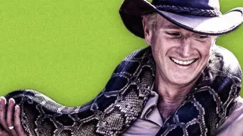 A smiling man in a hat holds a boa constrictor