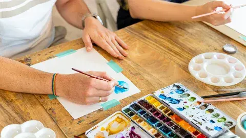 two individuals with watercolor paints at a table