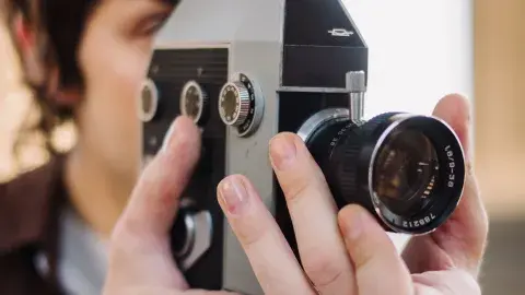 Closeup image of a person looking through the viewfinder of a vintage film camera and adjusting the lens.