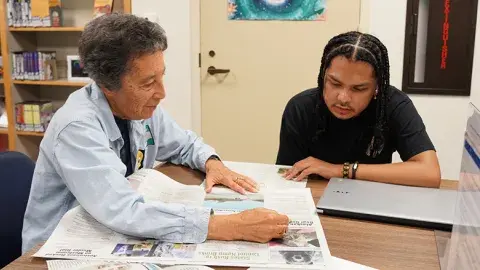 A woman and man sitting at a table reading a newspaper together