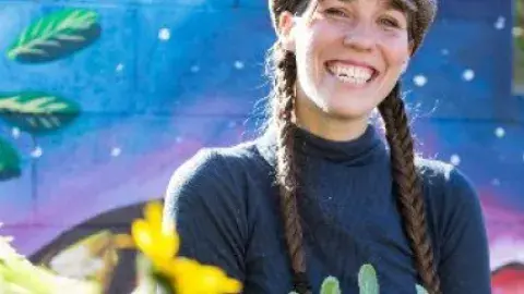Image of Brie Wakeland with long, brown braids, navy shirt, and a colorful background. 