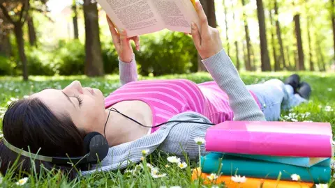 girl reading on grass with headphones 