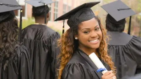 A group of college graduates, three are facing away from the camera and one is facing towards the camera smiling