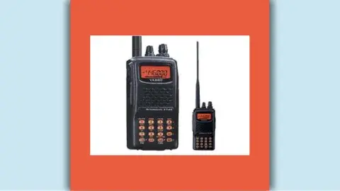 Two HAM radios, black with an orange screen, stand side by side. One is large and one is small.