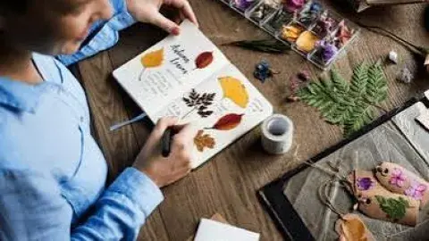 Person creating a nature journal with leaves and flowers.