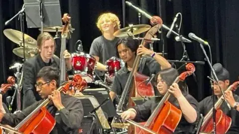 Diverse teenagers play cellos and the drums