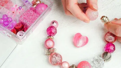 A pair of hands stringing beads into a bracelet.