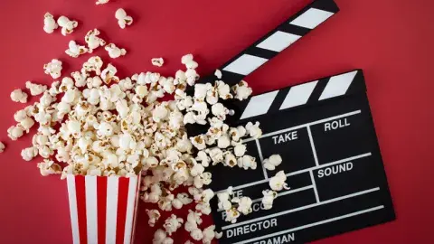 White and red popcorn bucket with popcorn next to a clapper board