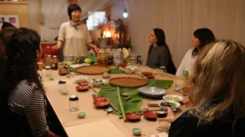 Jessica Wang standing at the head of a table surrounded by 4 adults listening to her instruction.