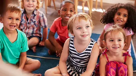 Group of young kids sit on floor rugs listening to a story