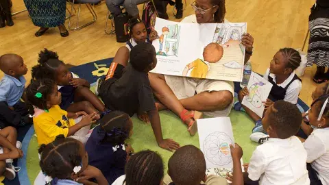 Woman holding an oversized book and reading to a group of children