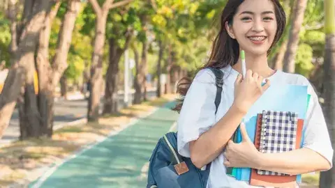 A student smiling on campus with backpacks and notebooks