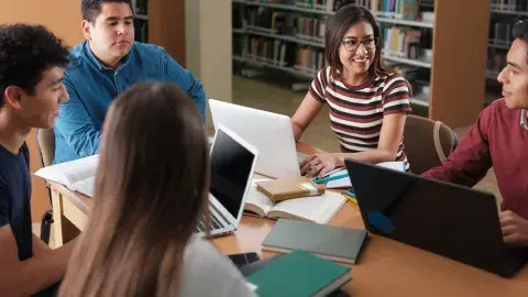 Five students sitting at a table, working with their laptops
