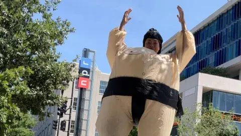 Person with upraised arms in inflatable sumo wrestler costume