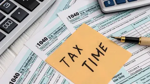  tax time written on a post-it note with tax paperwork, a pen and calculator in the background