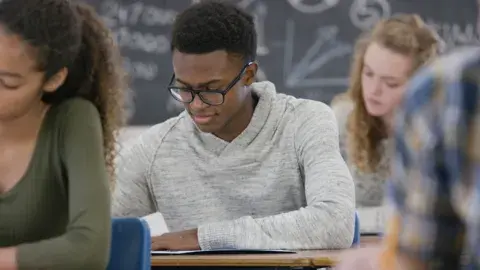 three teens sitting at desks in a classroom filling out test forms