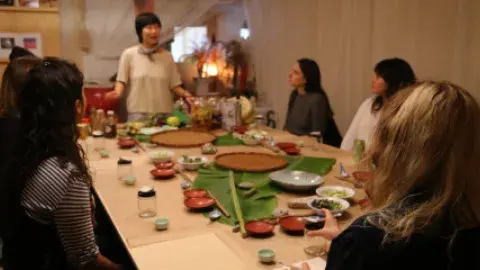 Jessica Wang standing at the end of a table with people around the table. Dishes and small jars are on the table.