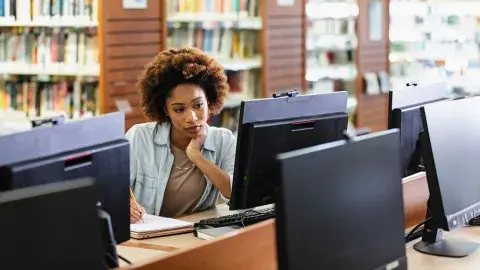 Woman taking notes while looking at a computer
