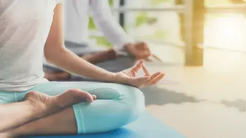 Two people seated on a floor in a yoga position with sunlight shining.
