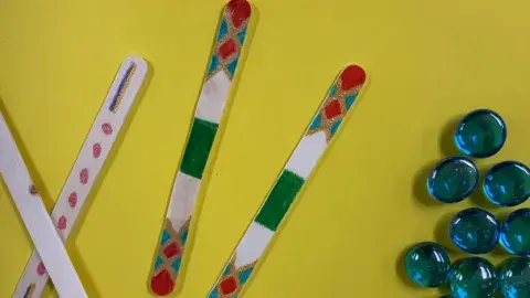 Four popsicle sticks with multicolored designs on them and a cluster of blue marbles