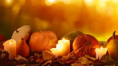 Autumn night scene with pumpkins, squash and lighted candles on fallen leaves
