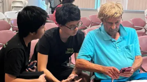 2 teens looking a a senior's phone