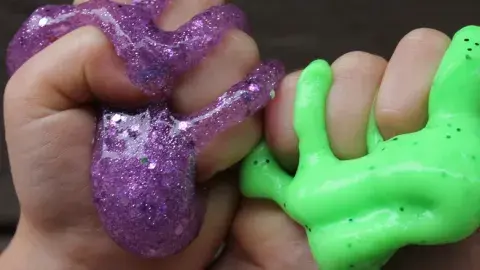 Two hands squishing purple and green slime. 