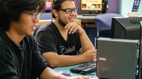 Two boys smiling and using desktop computers