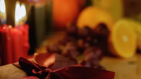 Red holiday candles and sliced fruits blurred out in the background with a gift with a red bow in the front.