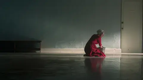 woman in red in a bonnet cleaning a big dark floor in an empty room